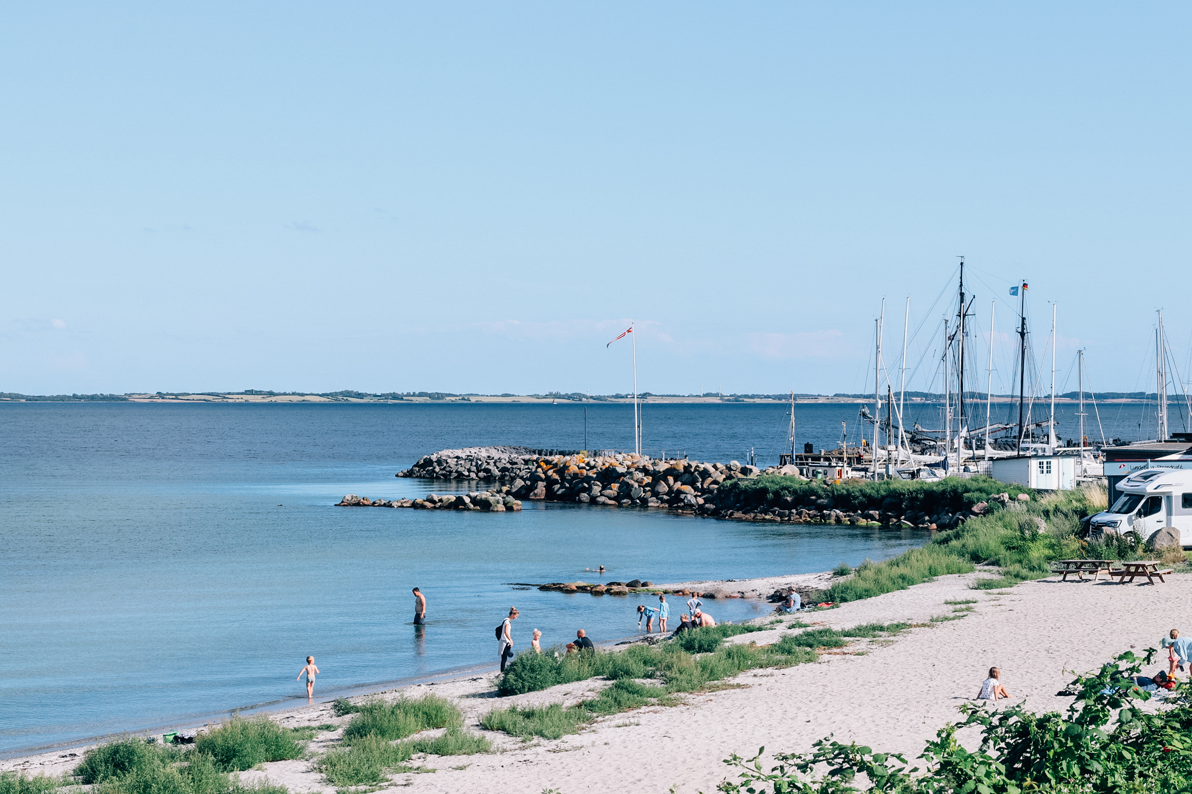 Strand med børn i vandet og lundeborg havn i baggrunden